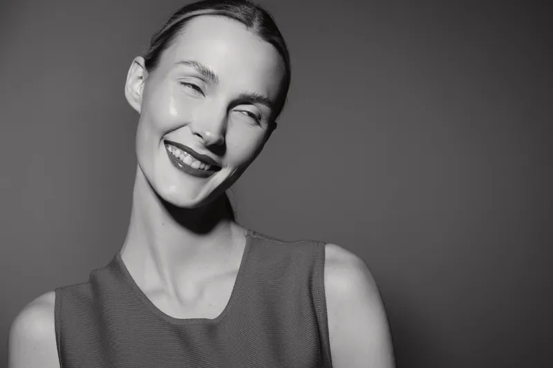 Smiling white woman with fair skin and slicked back hair poses in studio against dark background. Concept for happiness, beauty, and portrait photography.