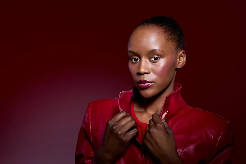 Confident black African woman with dark skin wearing a red leather jacket poses against a red background. Studio portrait with dramatic lighting and a strong, stylish mood.
