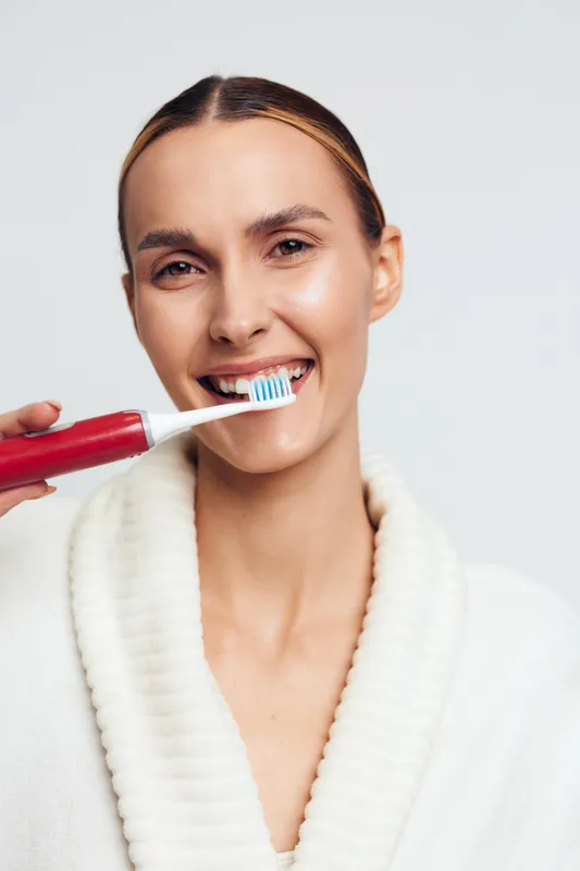 Smiling woman brushing teeth with electric toothbrush white background closeup healthy dental care hygiene morning routine clean smile wellness