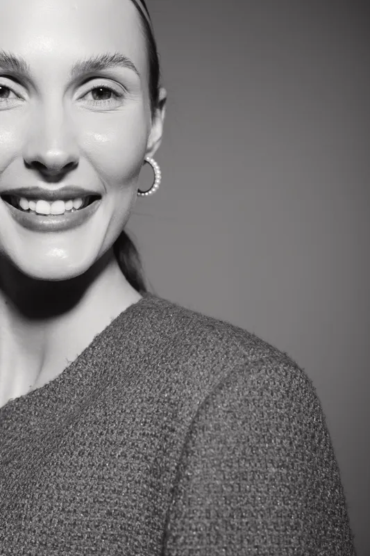 Smiling Caucasian woman with fair skin wearing textured sweater and hoop earrings, close-up portrait in black and white studio lighting.