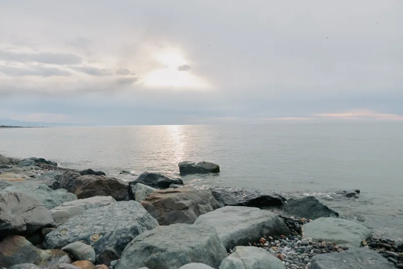 Rocky coastline under cloudy sky with calm sea water reflecting soft sunlight. Peaceful atmosphere of nature, ocean, and cloudy weather at the shore during daytime.