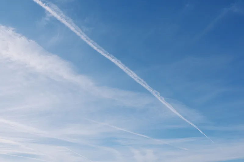 Clear blue sky with a diagonal white contrail across the atmosphere, wispy clouds and bright daylight, minimal aviation scene suitable for travel, nature, or freedom themes.