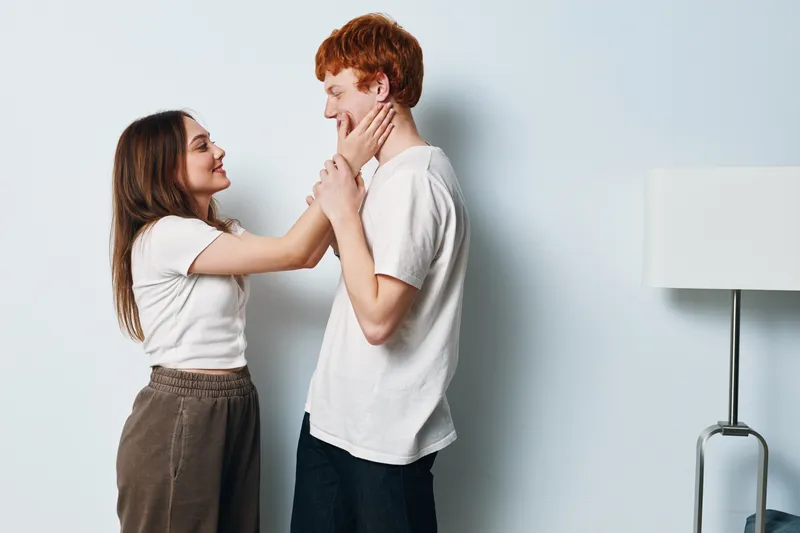 Couple, woman and man touching faces with gentle hands for affection and love at home. Young romantic relationship, smile and casual outfit for happiness and connection indoors.