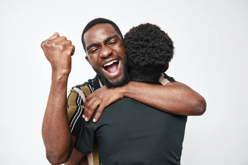 African American men with dark skin hugging and celebrating success together, showing happiness and friendship in casual clothing on white background.