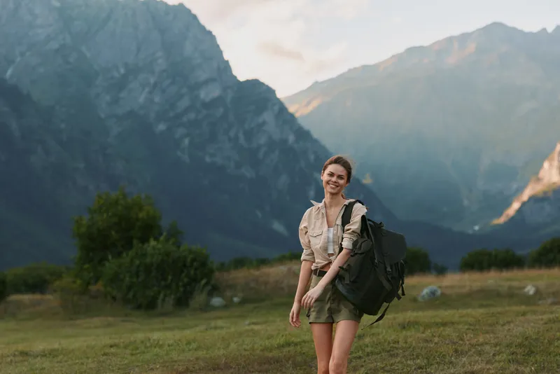 Young woman hiker with a backpack in a wide alpine valley, casual outdoor style, exploring nature under sunny skies with rugged mountains in the background, conveying outdoor