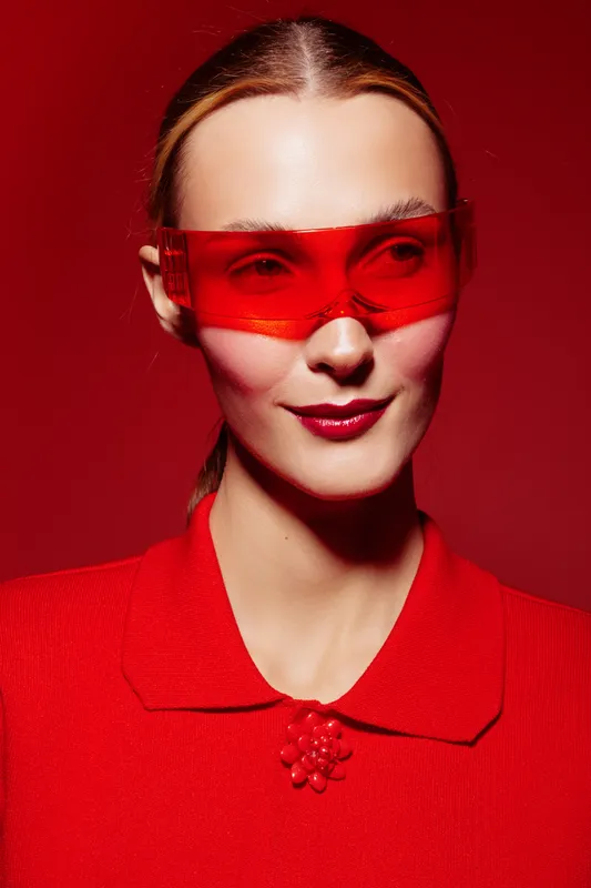 Portrait of a confident woman wearing red sunglasses and a red outfit against a red background. The image highlights fashion, style, and bold color contrast in studio lighting.