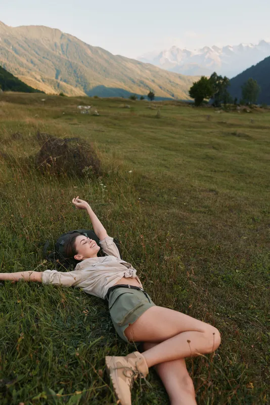 woman lifestyle outdoors field mountains relaxed sunlight playfulness nature breeze carefree casual portrait in a sunny meadow with warm tones and peaceful mood