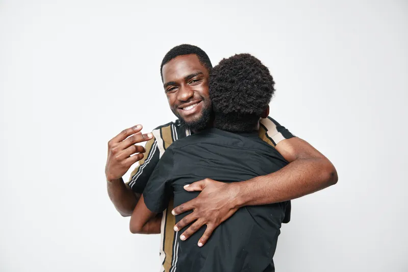 Two African American men hugging and smiling with dark skin and casual clothes on white background for friendship and connection. Happy black men embracing each other.
