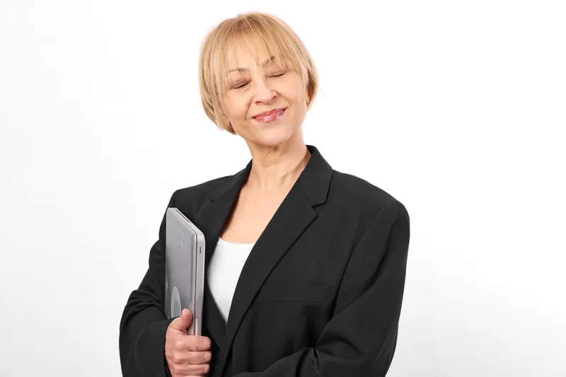 Woman senior business smartphone studio smiling white holding gesture, eyes closed, relaxed posture, black blazer, soft light, clean background, copy space