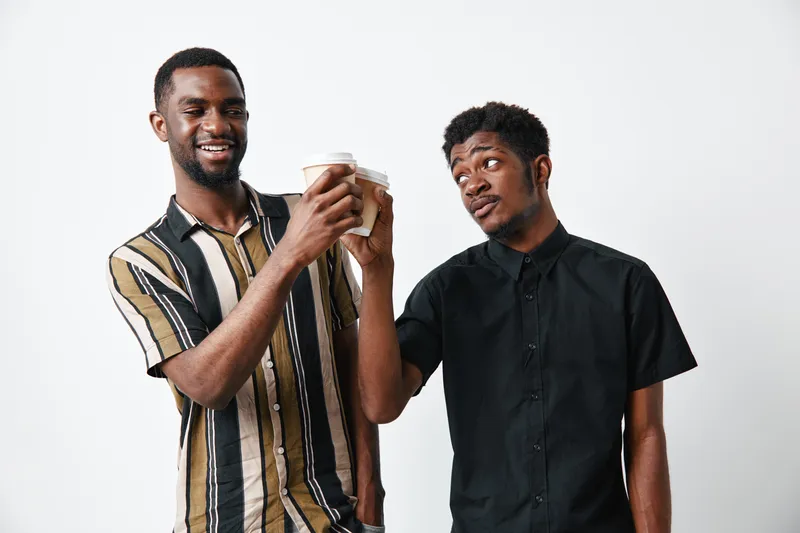 Two young black men with dark skin holding coffee cups and smiling on white background for friendship and casual lifestyle concept.