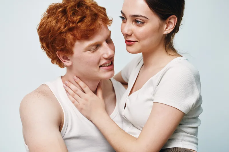 Couple with red hair man and woman in white top embracing each other for love relationship and affection in studio portrait. Intimate, young, smiling, affection and connection.