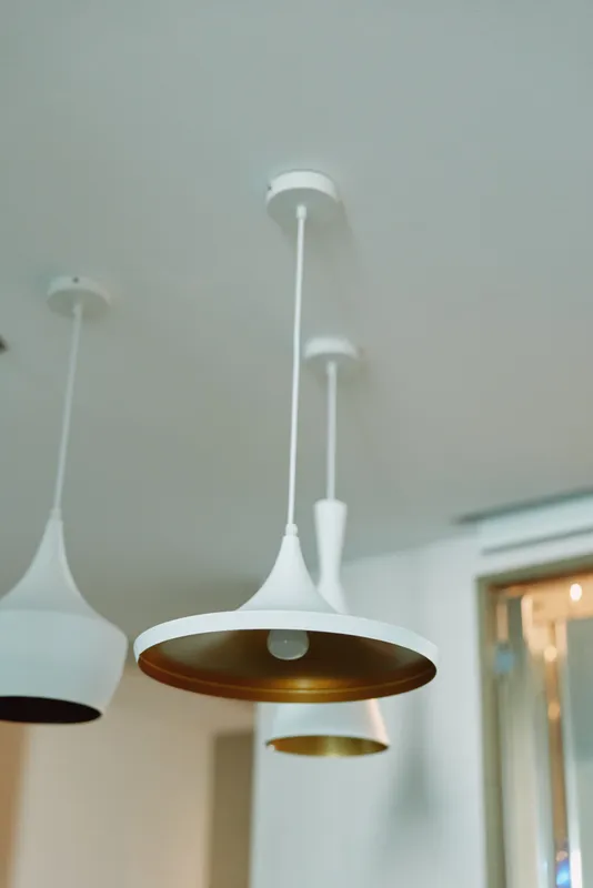 Modern white pendant lamps hanging from the ceiling over a clean, minimalist interior. Sleek fixtures with a warm glow create a contemporary vibe and balanced illumination in a bright living space.