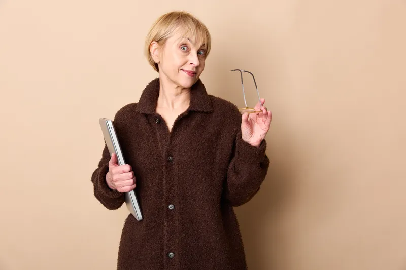elderly woman smartphone glasses beige studio portrait technology communication, handheld screen use, soft studio light, calm expression, indoor daily life, quiet mood