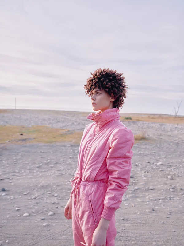 Person, fashion, pink jumpsuit worn by a model in an outdoor landscape with rocky ground and wide sky, showcasing bold color, contemporary style and natural light.