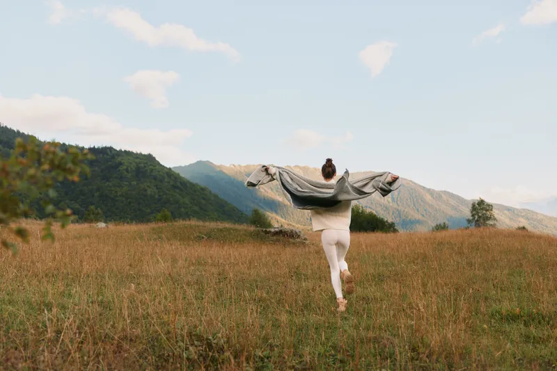 Woman lifestyle enjoying freedom running in open field with mountains in background on sunny day. Concept of nature, wellness, and outdoor activity with casual clothing.