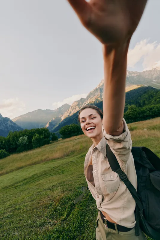 woman selfie hiking mountain outdoors nature backpack travel smile adventure lifestyle portrait in scenic meadow during sunny day joyful traveler posing with arm extended for a candid shot