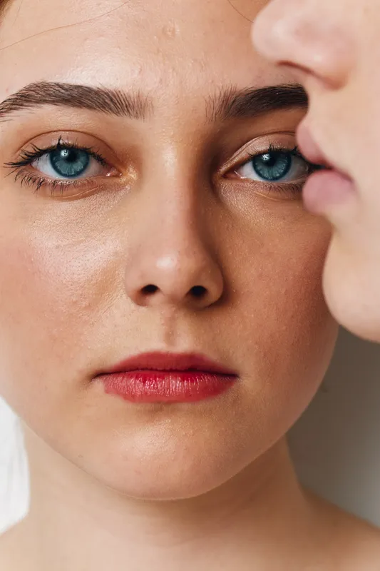 Portrait of a woman with blue eyes and red lips looking straight ahead, closeup of natural skin texture and detailed facial features with soft lighting.