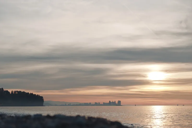 Sunset over a calm sea with a distant coast and soft clouds, warm glow on the water creates a tranquil landscape for nature, travel and reflective moments