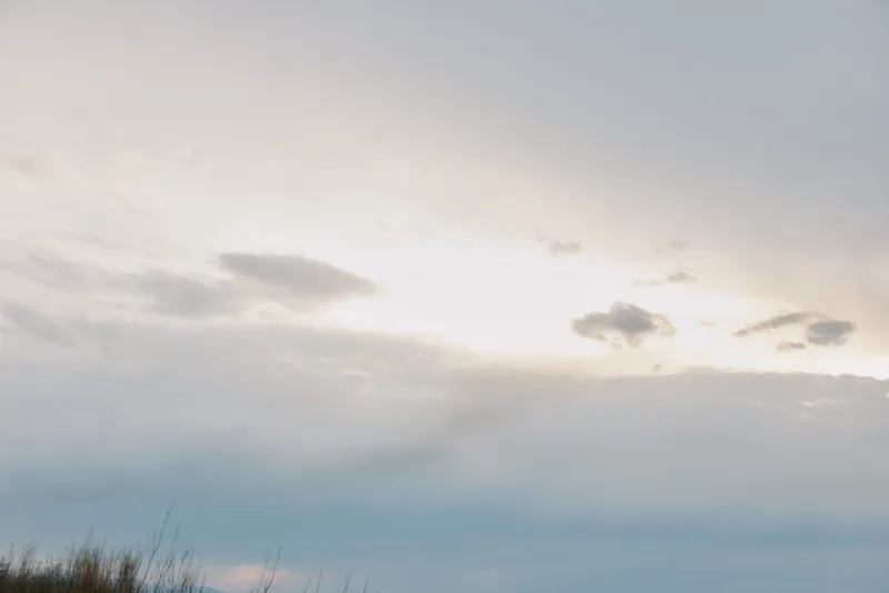 Calm cloudy sky with soft light above horizon and grass silhouette. Peaceful nature scene with light clouds and serene atmosphere at dusk or dawn.