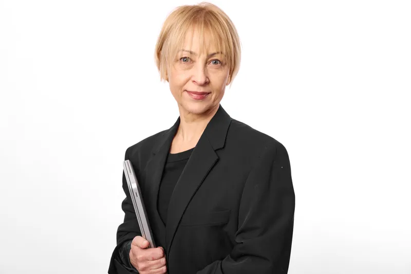 Elderly woman in black blazer holding folder in studio portrait, calm business professional on white background, representing education and mentorship, career success.