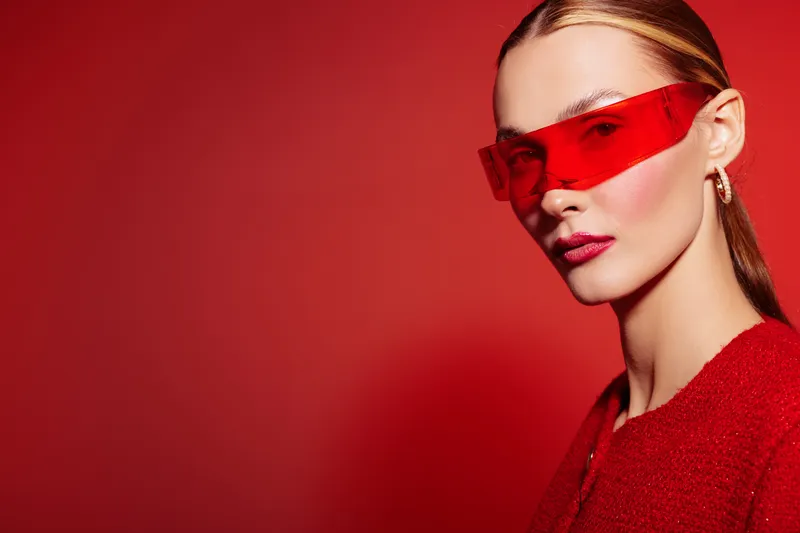 Portrait of a stylish woman wearing red sunglasses and a red outfit against a red background. Concept of fashion, modern style, and bold color contrast in studio lighting.