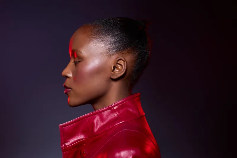 Profile of a dark skinned African woman with smooth skin wearing a red leather jacket against a dark background. Concept of fashion, beauty, elegance, and confident style.