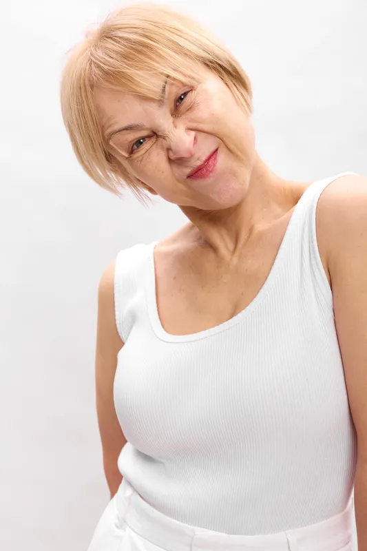 Woman blonde portrait in studio, white vest on a white background, eyes closed, showing fatigue and pain, gentle beauty expression, soft light, neutral mood