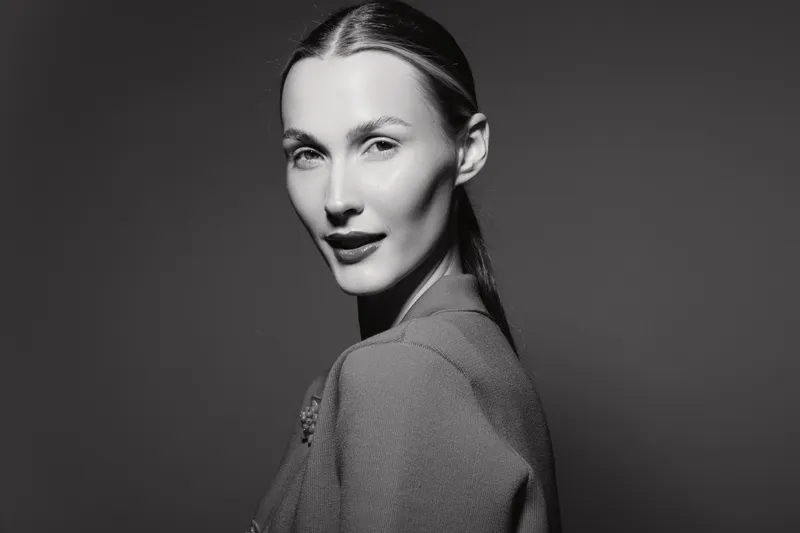 Portrait of a white woman with pale skin and sleek hairstyle wearing textured clothing on dark background. Concept of fashion, elegance, and monochrome beauty.