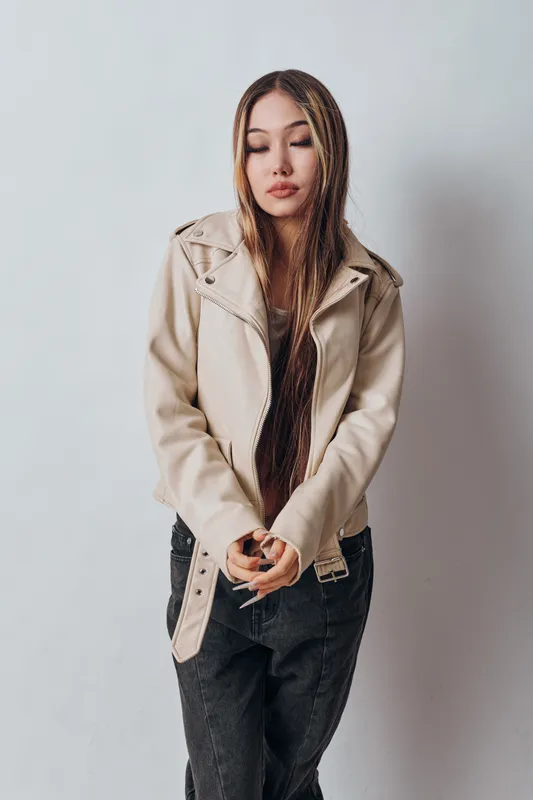 Young woman with long braids wearing a beige jacket and dark pants standing with closed eyes isolated on white background in studio portrait.
