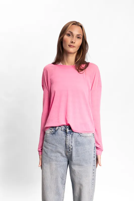 Young woman wearing pink sweater and blue jeans stands against white background. Casual fashion outfit concept with natural light and relaxed mood. Female model posing confidently.