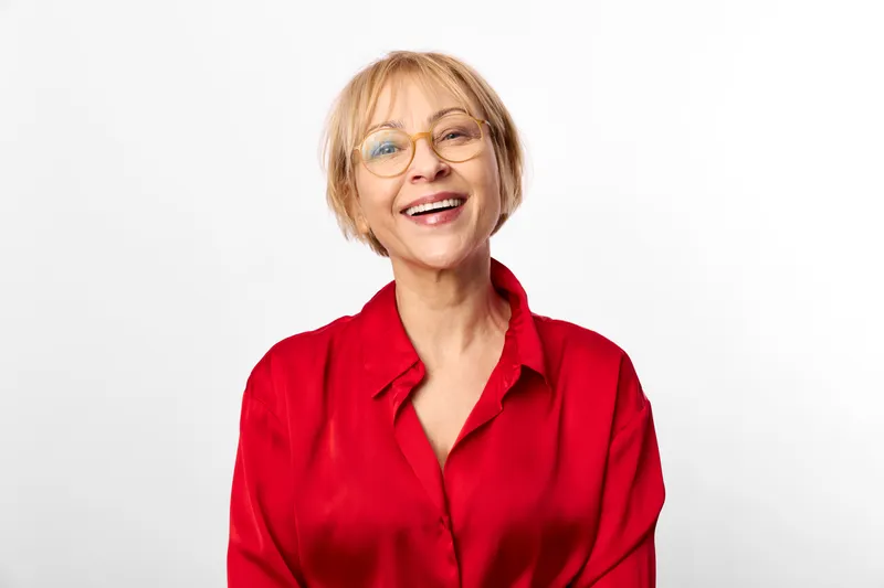 Woman portrait glasses smile elderly red blouse, studio headshot on white background, cheerful senior looking at camera, warm confident expression, casual lifestyle, soft light
