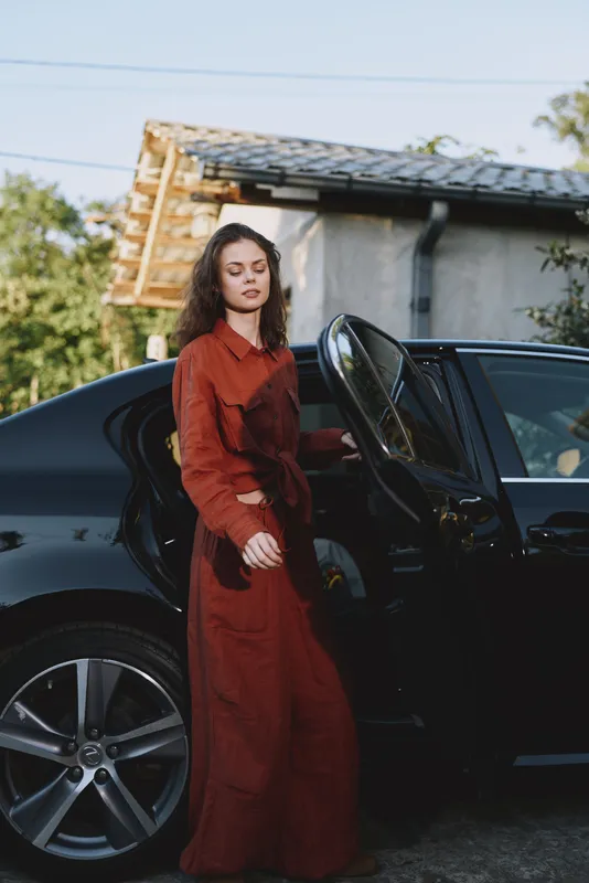 Woman lifestyle outdoors, wearing a red dress, stepping from a sleek car, confident pose, sunlit scene, natural colors, urban backdrop, candid moment