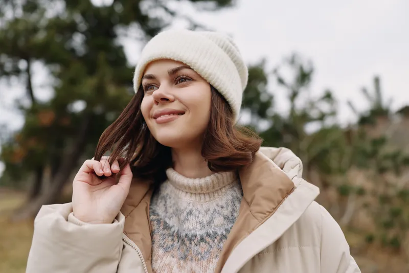 Woman in a warm coat and beanie outdoors, winter portrait in a park setting, cozy knit sweater, soft natural light, relaxed expression and gentle breeze