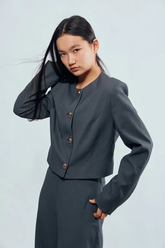 Young woman posing in gray fashion outfit with long hair, looking confident and stylish against light background. Female model wearing modern knitwear jacket and pants in studio.