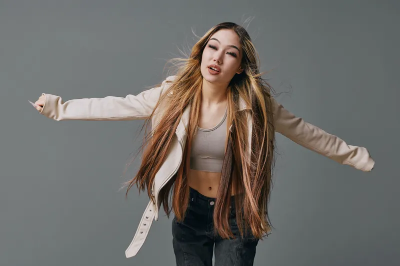 Woman with long hair and casual clothing posing expressively with arms extended on plain background, fashion style with relaxed mood and natural beauty sense.