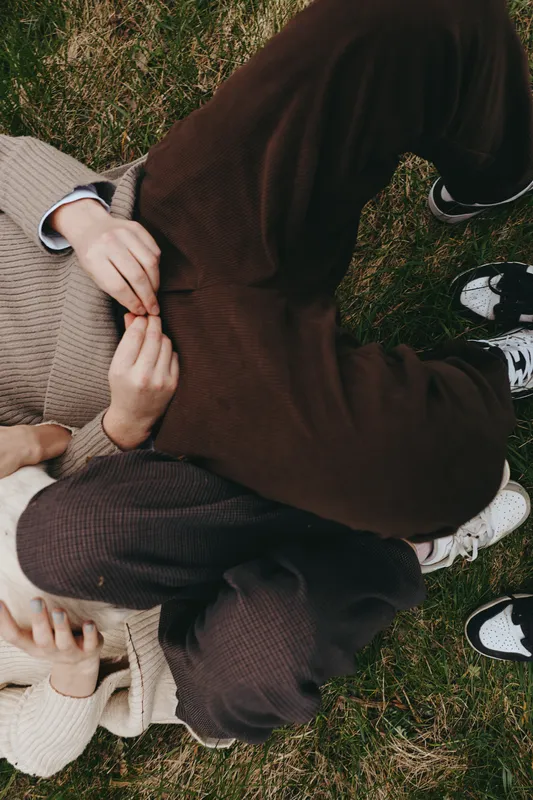 Couple, outdoors, grass, casual, cozy, friendship, relaxation, sweater two people sit on grass in knitwear enjoying a warm moment outdoors, showcasing lifestyle, connection, and casual fashion