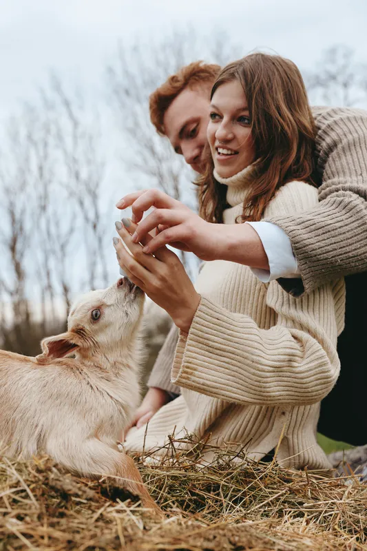 Joyful couple outdoors sharing a playful moment with a dog, warm sweaters, soft light, natural tones, lush grass, candid interaction, relaxed happiness, outdoor lifestyle and nature scenery
