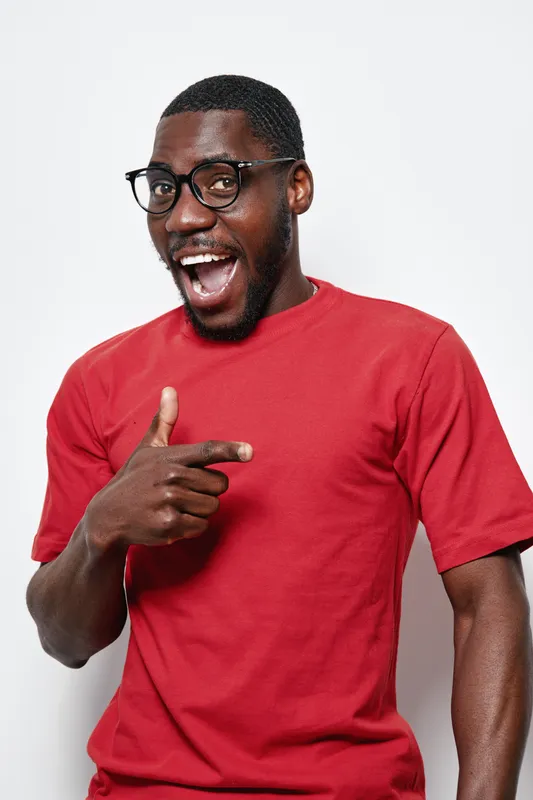 African American man with dark skin wearing glasses and red t shirt smiling and pointing finger on white background. Happy male portrait with casual style and positive expression.
