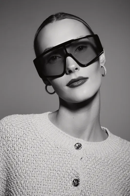 Stylish caucasian woman with pale skin wearing oversized sunglasses and white textured sweater in studio light.