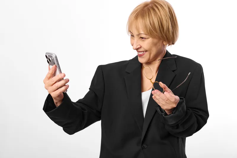 Smiling woman in business suit using smartphone, portrait with phone in hand, clean white studio background, concept of communication, mobile technology, professional lifestyle, warm friendly mood
