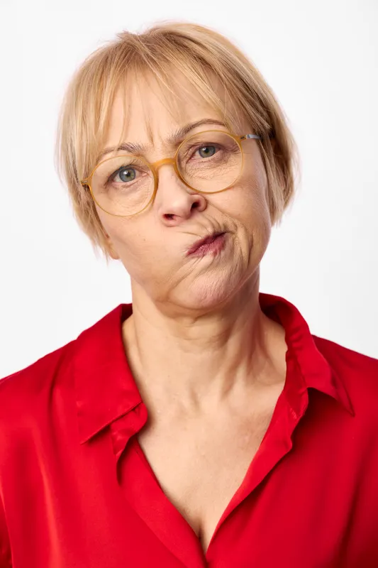 Smiling senior woman with glasses, short blonde hair, studio portrait on plain white background, wearing a red shirt, closeup friendly expression, concept of age grace care