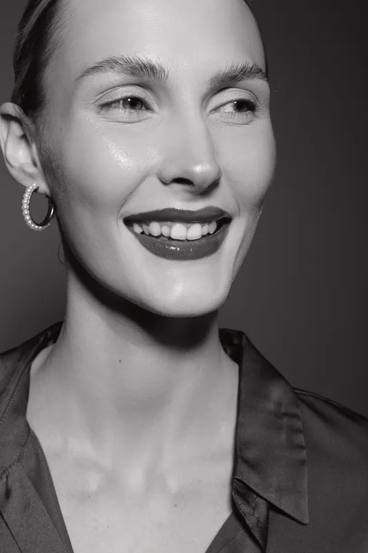Smiling Caucasian woman with fair skin and short hair wearing pearl hoop earrings and dark blouse. Concept of happiness, beauty, and natural elegance in black and white portrait.