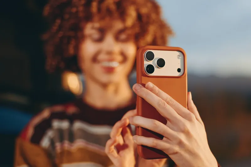 Woman outdoor lifestyle selfie, hands holding smartphone close to face, curly hair and earrings, soft evening bokeh background, casual candid portrait, modern technology moment, relaxed smile,