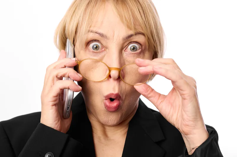 Woman surprised phone glasses blonde office communication shock, holding phone to ear, glasses framing face, wide eyes and open mouth, startled businesswoman