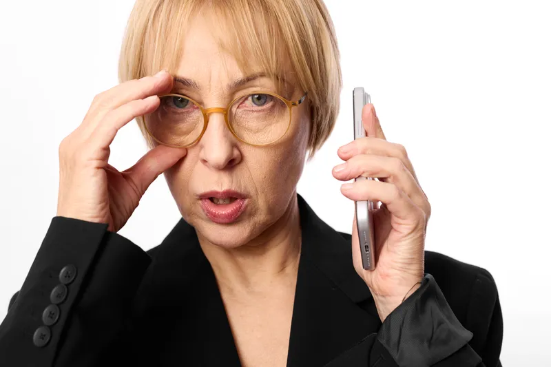 Woman with glasses in office portrait, blonde business professional holding phone to ear, adjusting frames, stress and surprise, corporate call, white background