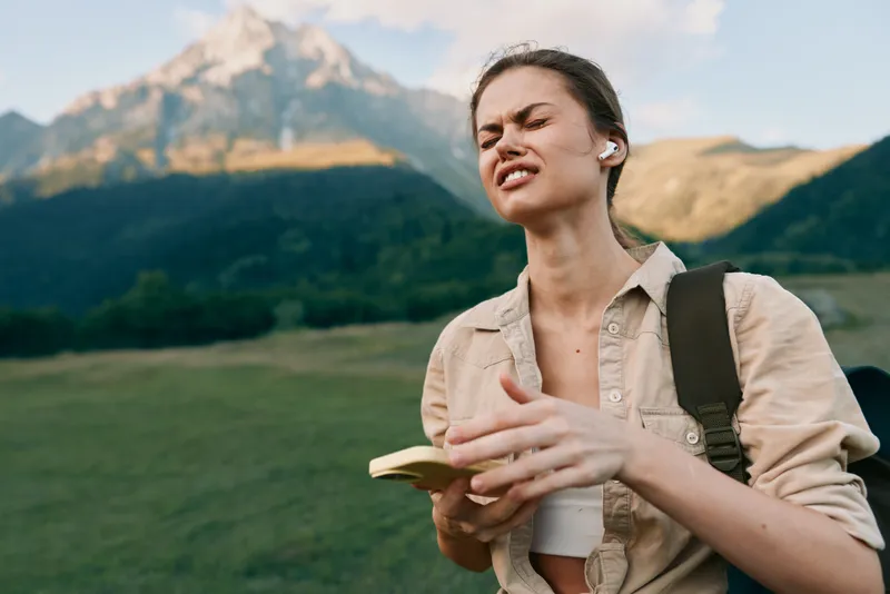 Young woman outdoors in mountains holding a map with eyes closed, enjoying nature, casual outfit, backpack, sunny day, peaceful expression, lifestyle concept