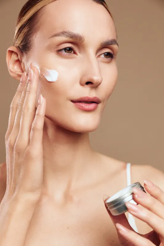 Woman applies cream on face for skincare beauty treatment, holding a jar while moisturizing skin with soft texture. Closeup portrait, cotton touch, calm spa routine and hydration concept.