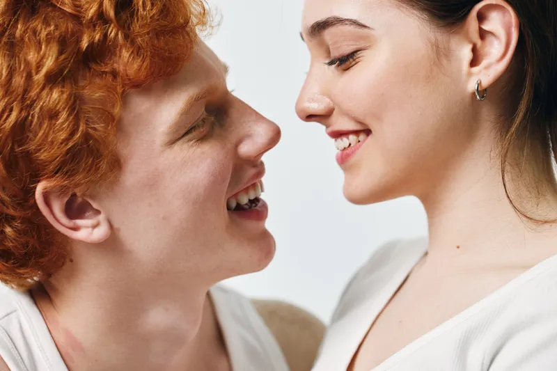 Couple, smiling and looking at each other with happiness and affection closeup. Young man and woman in white clothing with natural light and positive emotions on faces.