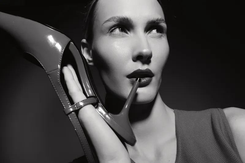 Closeup of a white woman with fair skin holding a high heel shoe near her face in black and white. Concept of fashion, style, and elegance in studio lighting.