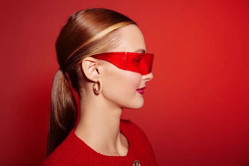 Profile of a stylish woman with red sunglasses and red sweater against a red background. Concept of fashion, modern style, and bold color contrast in portrait photography.